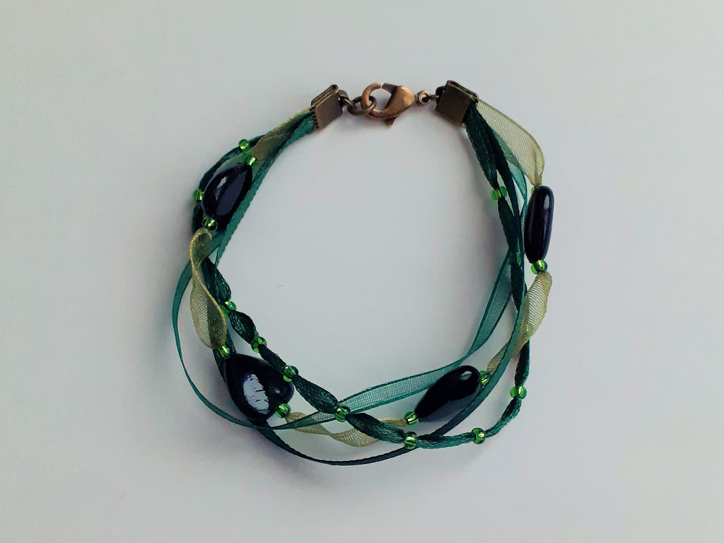 Bracelet Syléra : Trois rubans aux nuances de vert entrelacés, ponctués de perles et de cœurs profonds, pour une élégance naturelle et lumineuse au poignet.