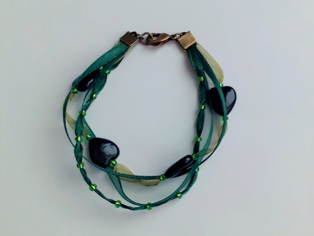 Bracelet Syléra : Trois rubans aux nuances de vert entrelacés, ponctués de perles et de cœurs profonds, pour une élégance naturelle et lumineuse au poignet.