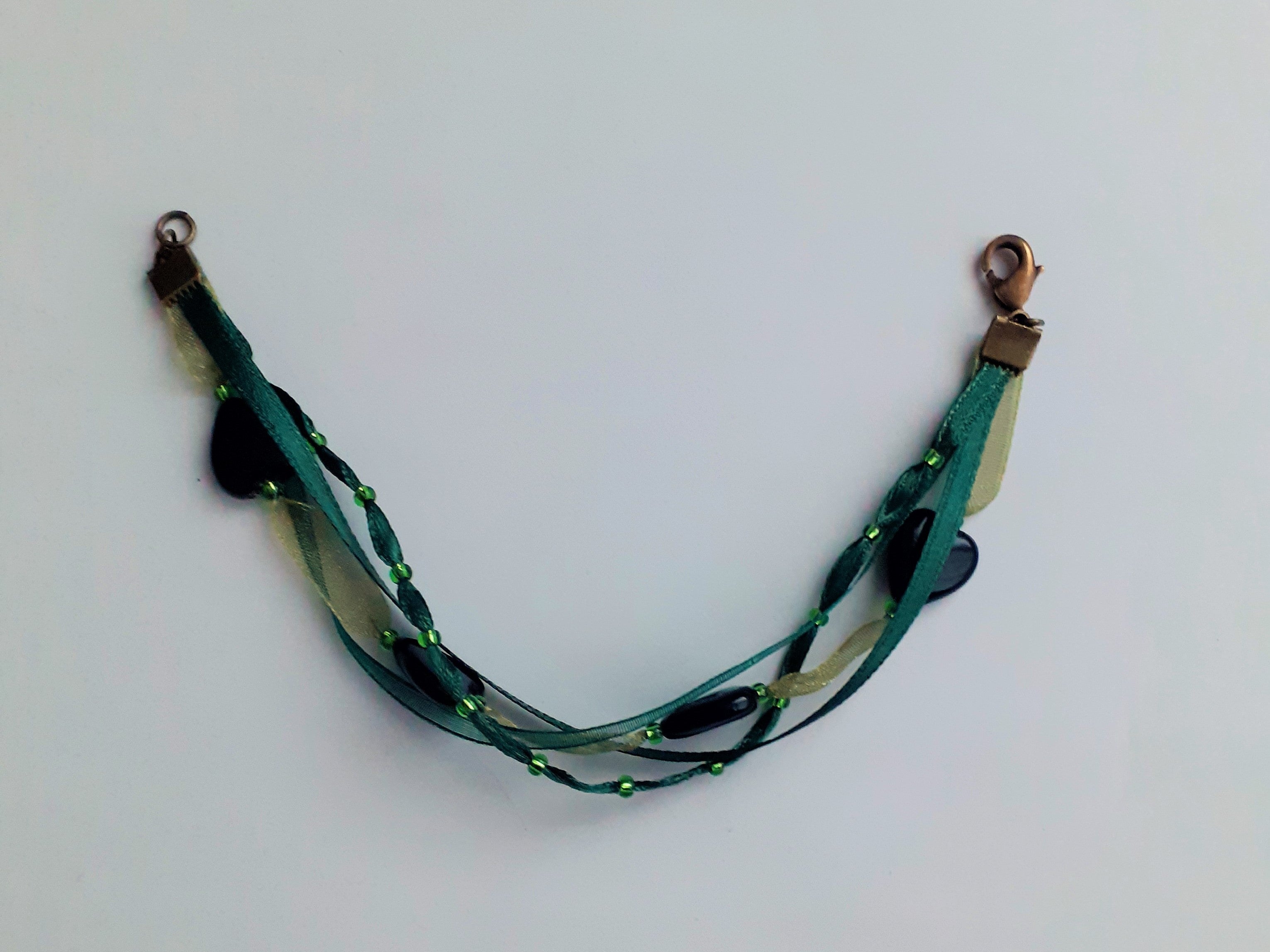 Bracelet Syléra : Trois rubans aux nuances de vert entrelacés, ponctués de perles et de cœurs profonds, pour une élégance naturelle et lumineuse au poignet.
