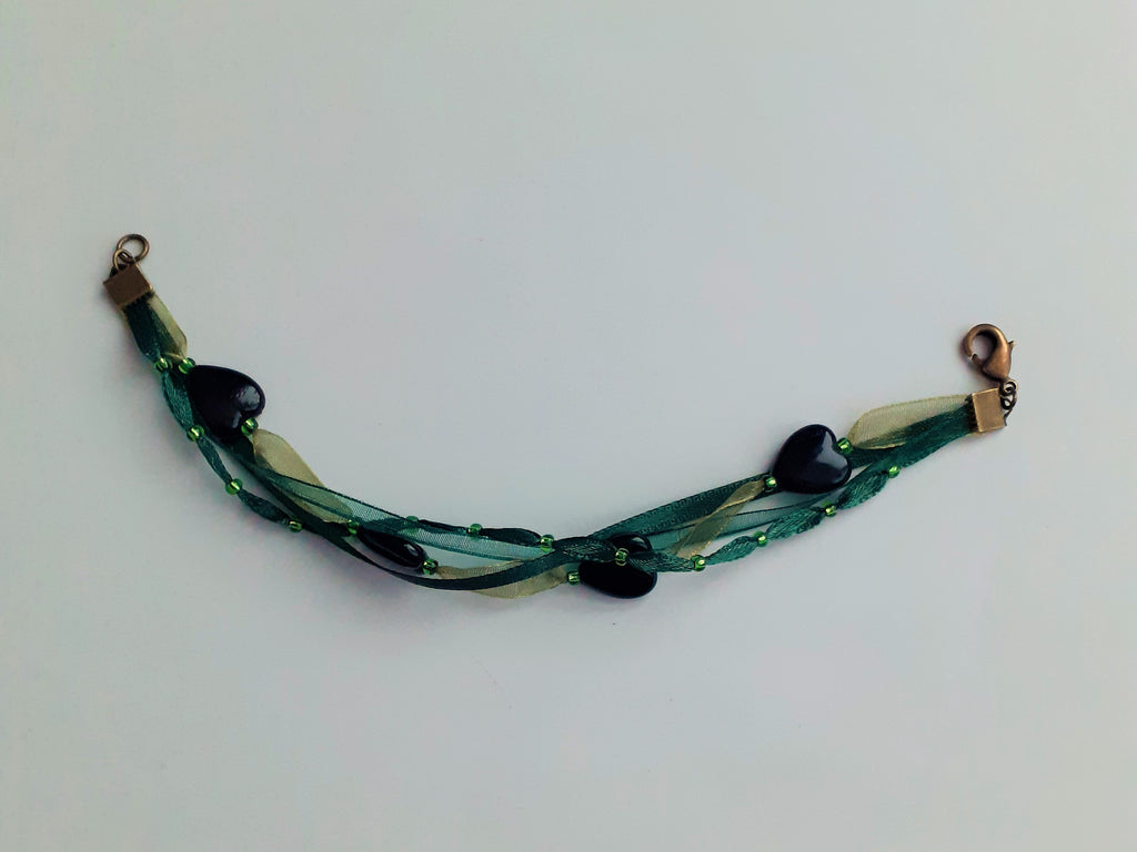 Bracelet Syléra : Trois rubans aux nuances de vert entrelacés, ponctués de perles et de cœurs profonds, pour une élégance naturelle et lumineuse au poignet.