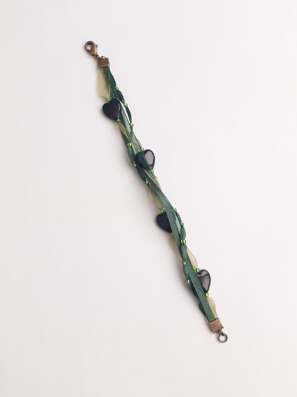 Bracelet Syléra : Trois rubans aux nuances de vert entrelacés, ponctués de perles et de cœurs profonds, pour une élégance naturelle et lumineuse au poignet.